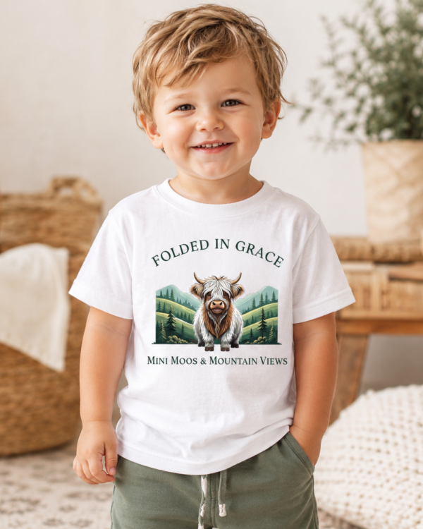 Toddler wearing the Mini Moos & Mountain Views white Highland cow graphic tee by Folded in Grace