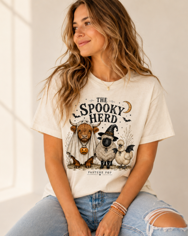 Woman wearing The Spooky Herd Halloween Tee featuring a Highland cow, sheep and chicken in playful Halloween costumes.